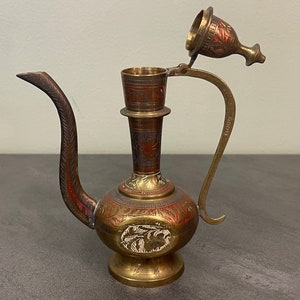 May include: A brass teapot with a decorative floral design and a removable lid. The teapot has a spout and a handle. The teapot is decorated with red, blue, and gold paint.