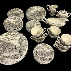 May include: A collection of vintage brown and white china with a pastoral scene. The set includes plates, saucers, cups, a gravy boat, a creamer, and a sugar bowl. The plates vary in size and shape, with a detailed landscape design.