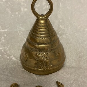 May include: A brass bell with a decorative design and a loop handle. The bell has a textured surface and a conical shape.