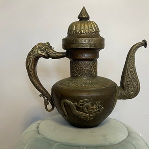 May include: An antique brass teapot with a dragon-shaped handle and spout. The teapot has intricate carvings and a domed lid.