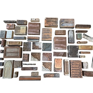 May include: A collection of various rectangular and square metal and wood printing blocks of different sizes. The blocks feature engraved text, decorative patterns, and illustrations, with some showing signs of wear and oxidation on the surfaces.