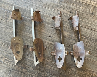 May include: Four vintage ice skate blades with wooden bases. The blades are made of metal and have a rusty patina. The blades are attached to the wooden bases with metal screws. The blades have a cross-shaped opening in the center.