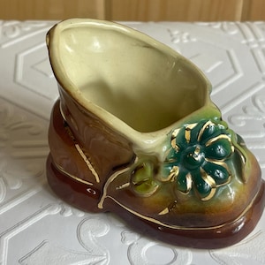 May include: A brown ceramic planter shaped like a shoe with a green and gold flower design.