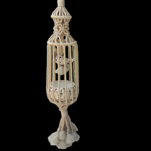 May include: A macrame plant hanger with a white ceramic pot and a decorative bird figurine. The hanger is made of natural cotton rope and has a tassel at the bottom.