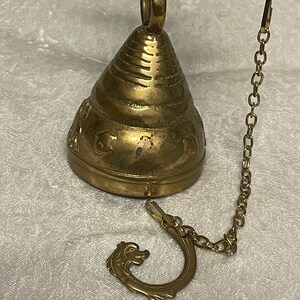 May include: A brass bell with a decorative design and a chain attached to a dragon-shaped hook.