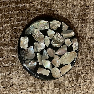 May include: A round black coaster with a design of iridescent white and gray seashells embedded in the surface.