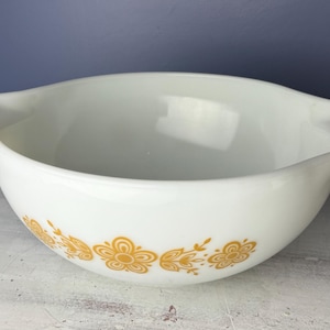 May include: White vintage mixing bowl with two handles and a floral pattern in shades of yellow. The bowl is made of ceramic and is ideal for mixing ingredients or serving food. The bowl measures approximately 9 inches in diameter.