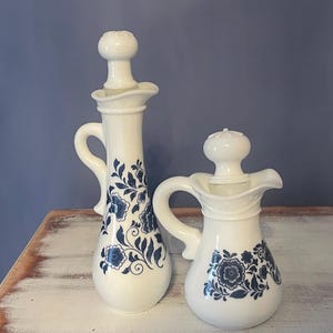 May include: Two white ceramic bottles with blue floral designs. The bottles have a vintage look and are perfect for displaying on a shelf or vanity.
