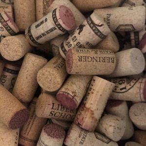 May include: A close-up of a pile of wine corks, many of which have the names of wineries printed on them. The corks are a mix of natural cork and synthetic cork.