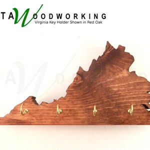 May include: A wooden key holder shaped like the state of Virginia. The holder is stained a dark brown color and has four gold hooks. The text "KATA WOODWORKING" and "Virginia Key Holder Shown in Red Oak" is visible at the top of the image.