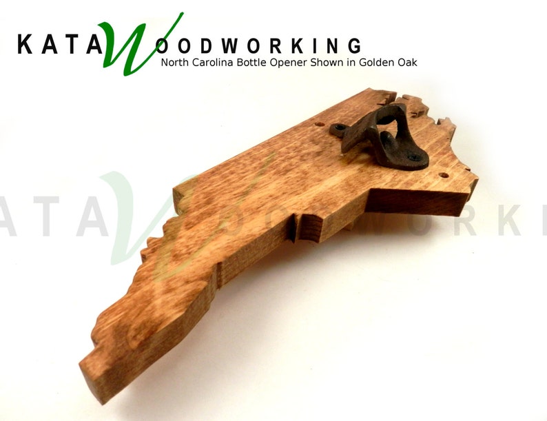 May include: A wooden bottle opener shaped like the state of North Carolina. The opener is made of golden oak wood and has a metal bottle opener attached to the top. The text "KATA WOODWORKING" is visible in the top left corner of the image. The text "North Carolina Bottle Opener Shown in Golden Oak" is visible below the logo.