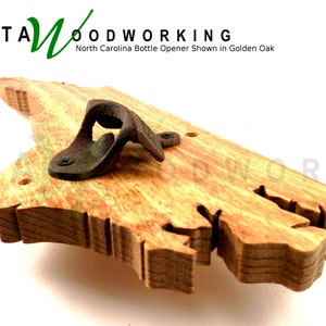 May include: A wooden bottle opener shaped like the state of North Carolina. The opener is made of golden oak wood and has a metal bottle opener attached to it. The text "KATA WOODWORKING" and "North Carolina Bottle Opener Shown in Golden Oak" is visible in the image.
