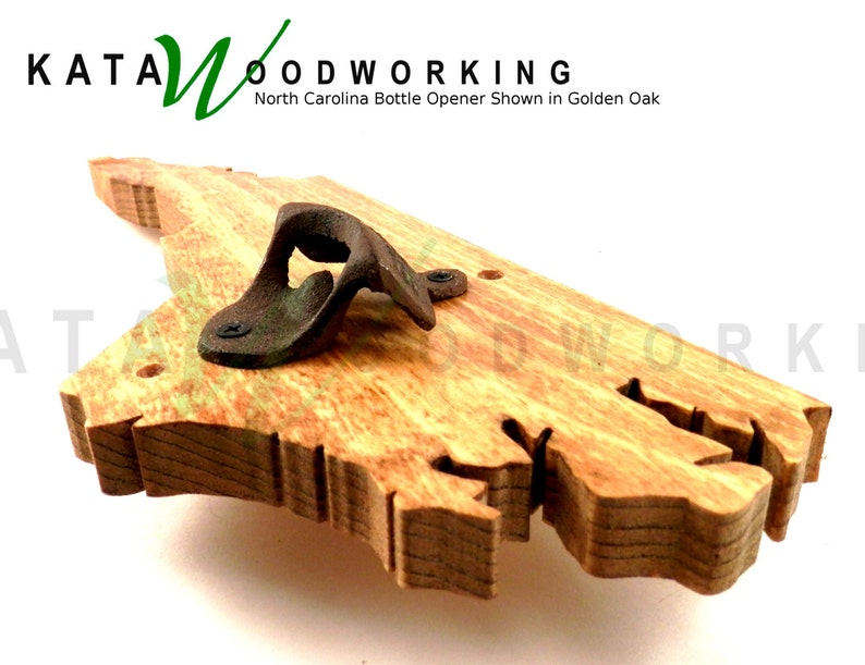 May include: A wooden bottle opener shaped like the state of North Carolina. The opener is made of golden oak wood and has a metal bottle opener attached to it. The text "KATA WOODWORKING" and "North Carolina Bottle Opener Shown in Golden Oak" is visible in the image.
