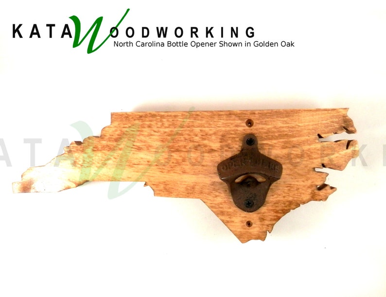 May include: A wooden bottle opener shaped like the state of North Carolina. The opener is made of natural wood with a rustic finish. The bottle opener is mounted on a wall. The text "KATA WOODWORKING" is visible in the top left corner of the image. The text "North Carolina Bottle Opener Shown in Golden Oak" is visible below the text "KATA WOODWORKING".
