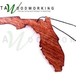 May include: A wooden ornament shaped like the state of Florida, stained in a reddish-brown color. The ornament is attached to a black string for hanging. The text "KATA WOODWORKING" and "Florida Ornament Shown in Red Oak" is visible in the image.
