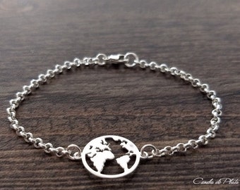 May include: A silver bracelet featuring a globe design. The bracelet has a chain-link style with a circular pendant cut out in the shape of the world. The bracelet is displayed on a dark wood surface.