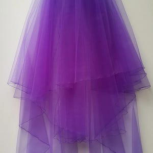 May include: A layered, sheer purple veil. The veil is made of a lightweight, flowing fabric, with multiple tiers creating a cascading effect. The edges are finished with a delicate trim. The veil is designed for bridal or formal wear.