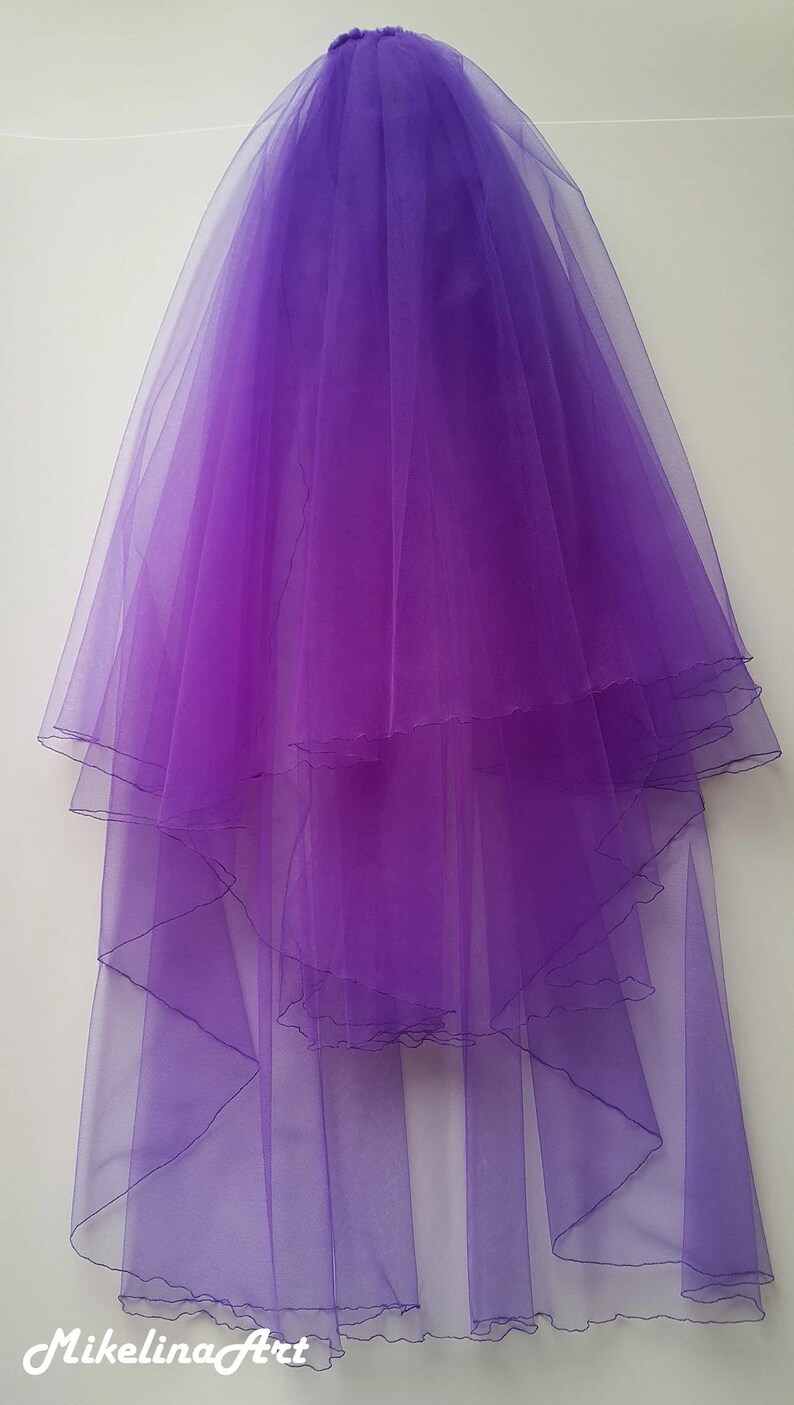 May include: A layered, sheer purple veil. The veil is made of a lightweight, flowing fabric, with multiple tiers creating a cascading effect. The edges are finished with a delicate trim. The veil is designed for bridal or formal wear.