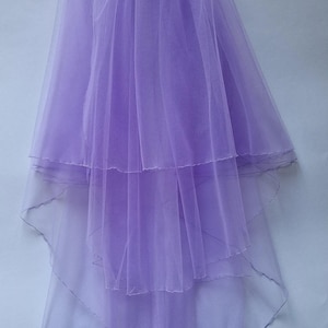 May include: A layered, lavender bridal veil. The veil is made of sheer fabric and features multiple tiers, creating a flowing effect. The bottom edges are gently scalloped. The Mikellina Art logo is visible in the bottom right corner.