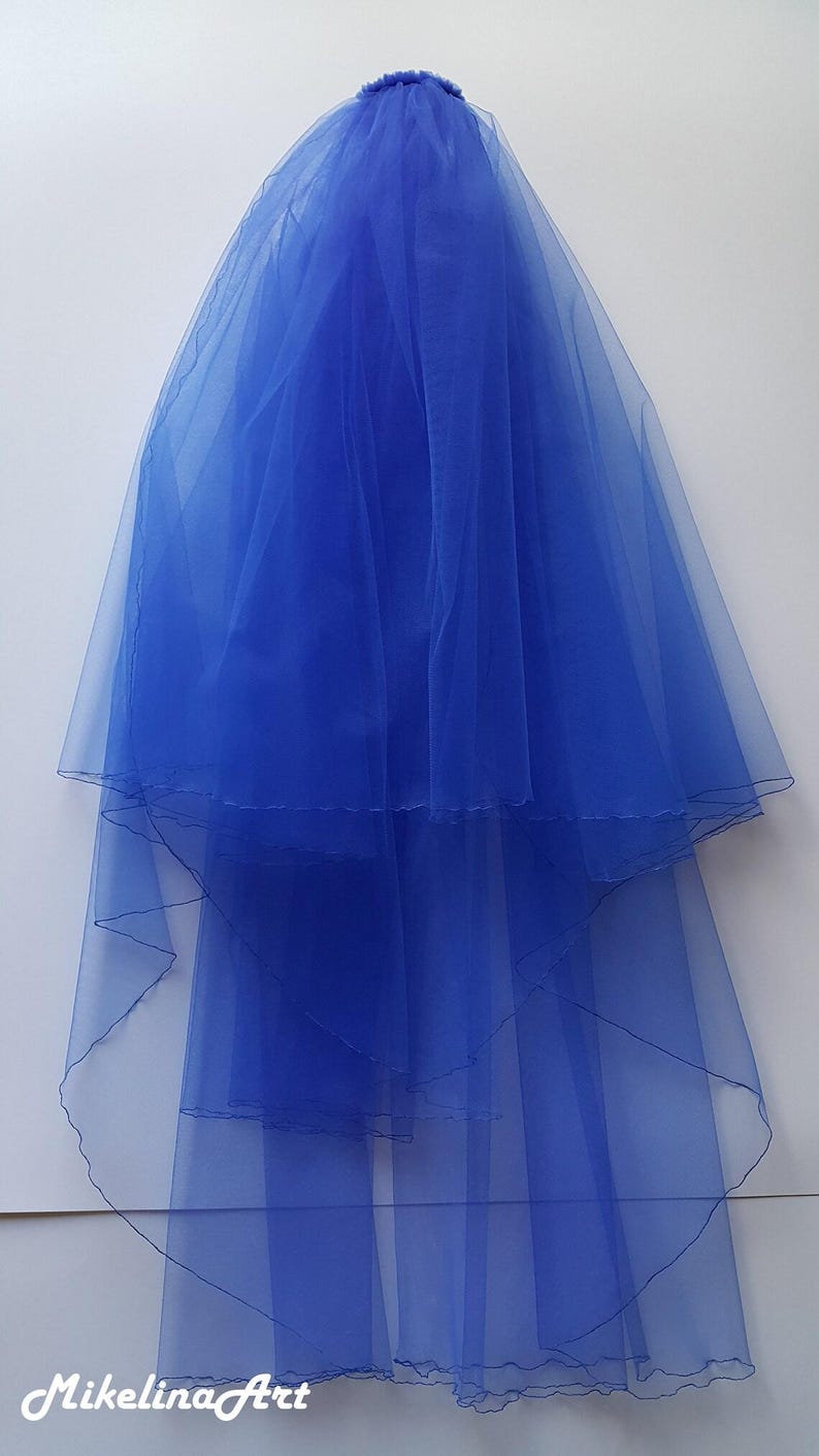 May include: A vibrant blue bridal veil, crafted from sheer fabric. The veil features multiple layers, creating a flowing, elegant silhouette. The veil is a bright, solid blue color, perfect for a wedding.