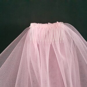 May include: A light pink bridal veil with a comb. The veil is made of a sheer, delicate fabric and is attached to a plastic comb. The text "MikelinaArt" is in the upper right corner. The background is a dark green.