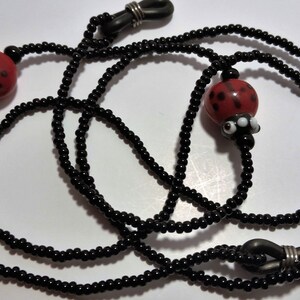 May include: Black beaded eyeglass chain with two red ladybug charms. The chain has silver metal clasps.