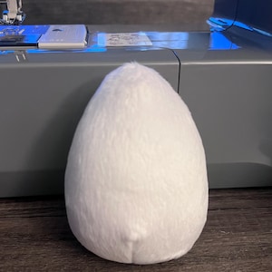 Pode incluir: Um brinquedo de pelúcia branco e felpudo em forma de ovo.
