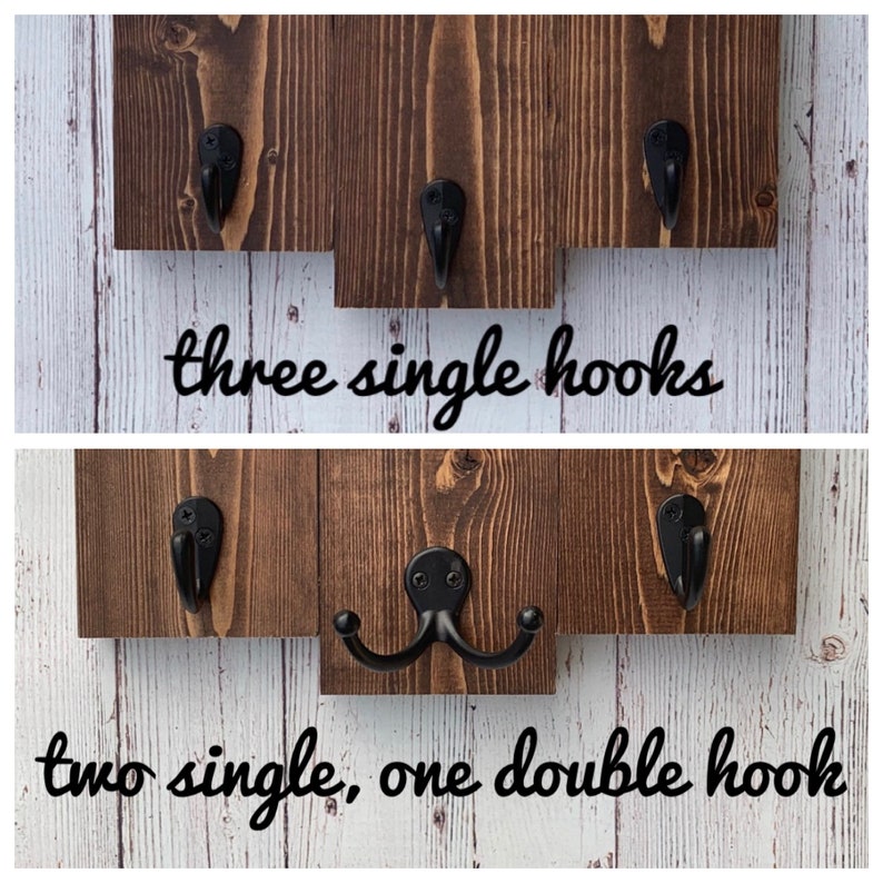 Op de afbeelding: Twee enkele haken en &eacute;&eacute;n dubbele haak gemonteerd op een houten plank. De plank is donkerbruin gebeitst. De haken zijn van zwart metaal.