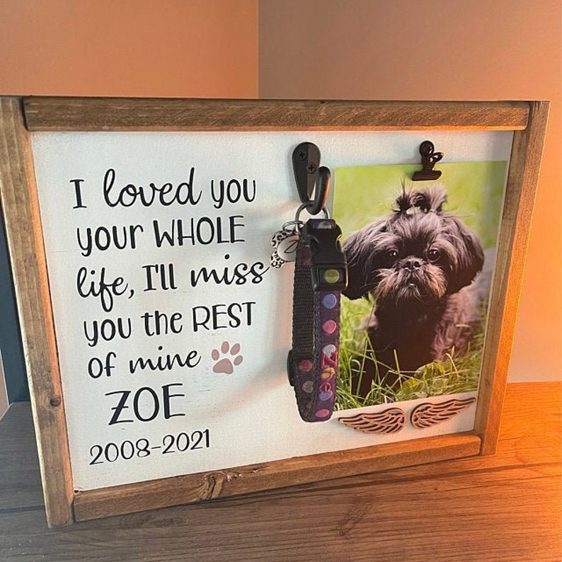 May include: A wooden framed memorial plaque with a black and white photo of a small black dog. The plaque has the text "I loved you your WHOLE life, I'll miss you the REST of mine ZOE 2008-2021".