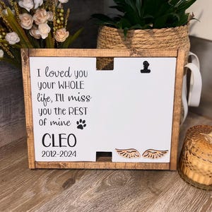 May include: A wooden sign with a white background and black text that reads "I loved you your WHOLE life, I'll miss you the REST of mine CLEO 2012-2024". The sign has a small paw print and two wooden angel wings.