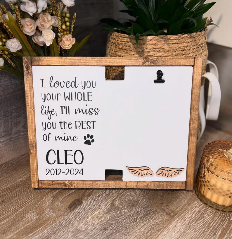 May include: A wooden sign with a white background and black text that reads "I loved you your WHOLE life, I'll miss you the REST of mine CLEO 2012-2024". The sign has a small paw print and two wooden angel wings.