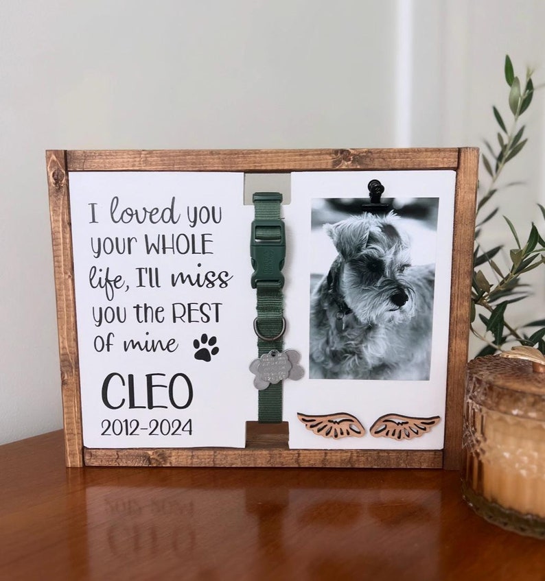 May include: A wooden memorial frame with a photo of a small dog, a green dog collar, a paw print, and the text "I loved you your WHOLE life, I'll miss you the REST of mine CLEO 2012-2024".