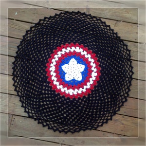 Pode incluir: Um tapete de crochê preto com uma estrela vermelha, branca e azul no centro. A estrela é cercada por um círculo de vermelho, branco e azul.