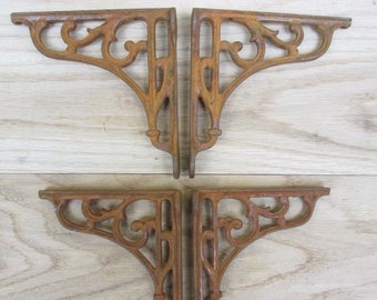Puede incluir: Cuatro soportes de estante de hierro fundido antiguos con un diseño decorativo de desplazamiento. Los soportes son de color marrón oxidado y tienen un aspecto desgastado.