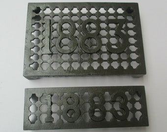 May include: Two black metal house number plaques with the number 1883 embossed on them. The plaques are made of a grid pattern.