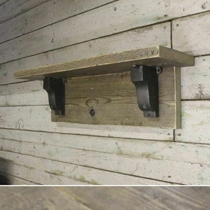 Puede incluir: Dos soportes de estante de metal negro con un diseño decorativo de desplazamiento. Los soportes están unidos a un estante de madera. Una regla se muestra en la segunda imagen para mostrar el tamaño del soporte.