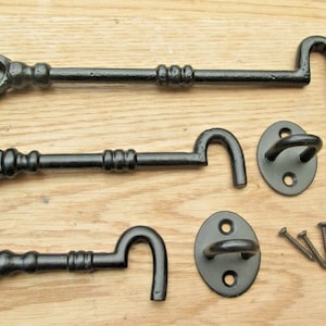 Könnte beinhalten: Drei schwarze Metall-Türriegel mit Haken. Jeder Riegel hat eine runde Platte mit zwei Schraubenlöchern. Die Riegel befinden sich auf einer Holzoberfläche mit Schrauben.