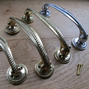 May include: A selection of decorative door handles in brass and silver. The handles have a curved design with a rope-like texture and a circular base. Screws are also visible, adding to the hardware aesthetic.