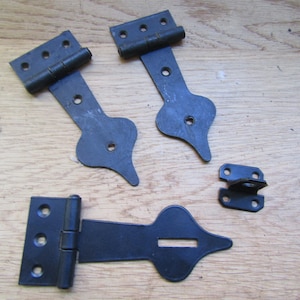 Puede incluir: Cuatro bisagras de metal negro con detalles decorativos. Las bisagras están diseñadas para usarse en puertas o portones.