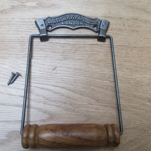 May include: Cast iron toilet paper holder with a wooden roller and a metal sign that reads "British Pip Paper Co. London".