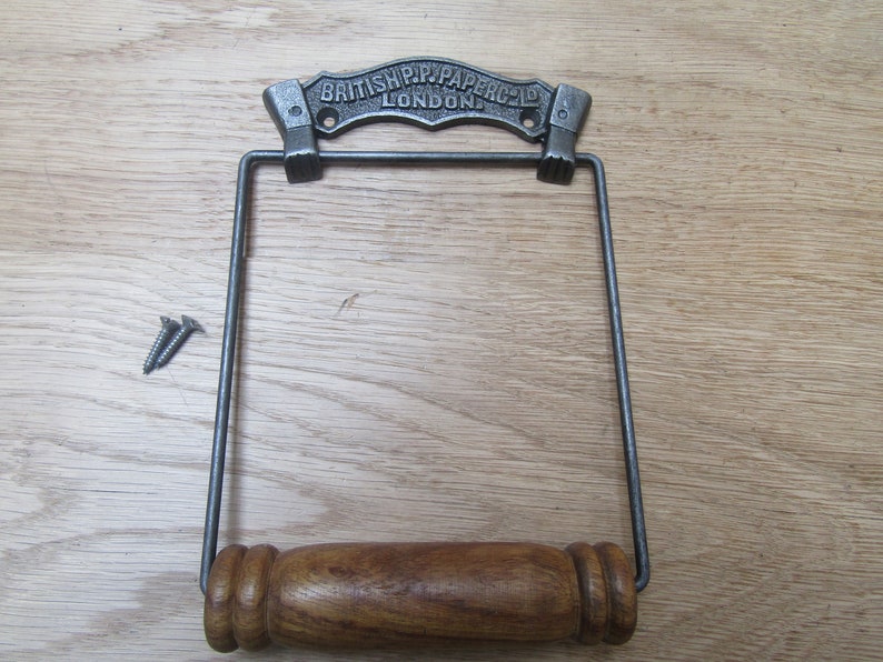 May include: Cast iron toilet paper holder with a wooden roller and a metal sign that reads "British Pip Paper Co. London".