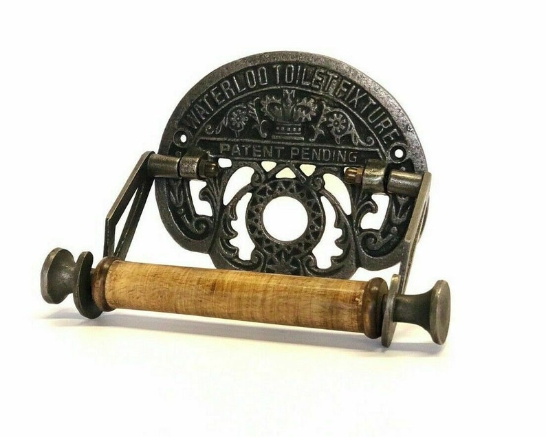 May include: Cast iron toilet paper holder with a wooden roller and a decorative design. The holder has the text "Waterloo Toilet Fixture Patent Pending" on the front.