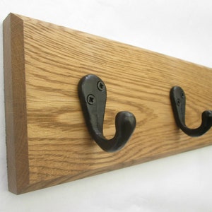 May include: A wooden coat rack with five black metal hooks. The rack is made of light brown wood with a natural grain pattern.