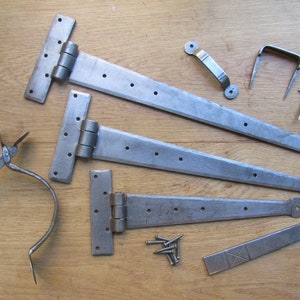 May include: Three pairs of long, silver-toned, metal hinges with rounded ends.  A silver-toned metal door handle, a silver-toned metal hook, and a silver-toned metal door stop are also included.  A small pile of silver-toned metal screws is in the centre of the image.