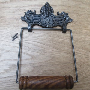 May include: A cast iron toilet paper holder with a decorative scroll design and a wooden roller. The holder is mounted on a wall with two screws.