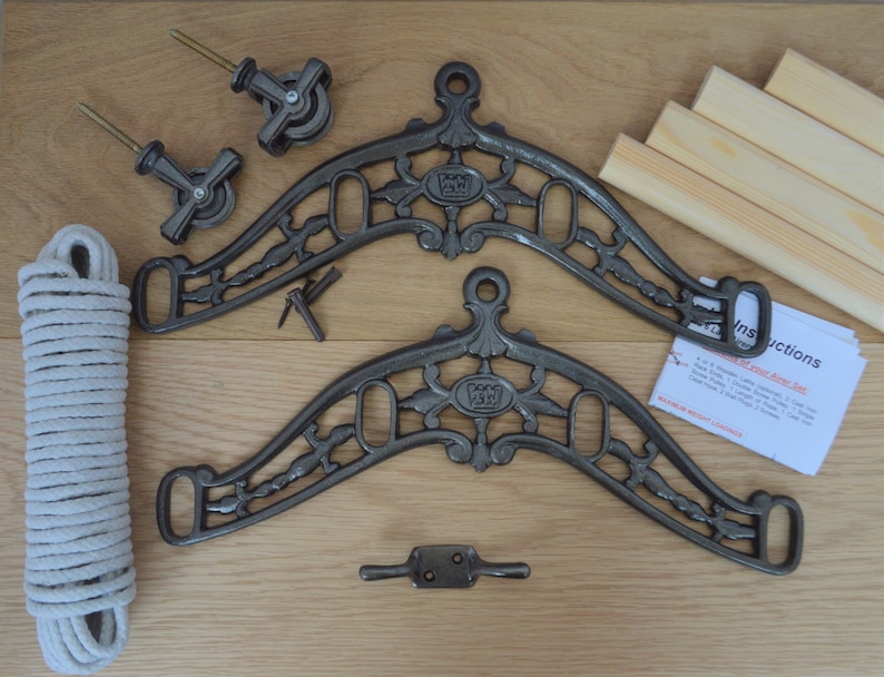 May include: An assortment of components for an airer set, including two ornate, gray metal brackets, wooden dowels, pulleys, and a length of white rope. Instructions are visible. The set is designed for indoor clothes drying.