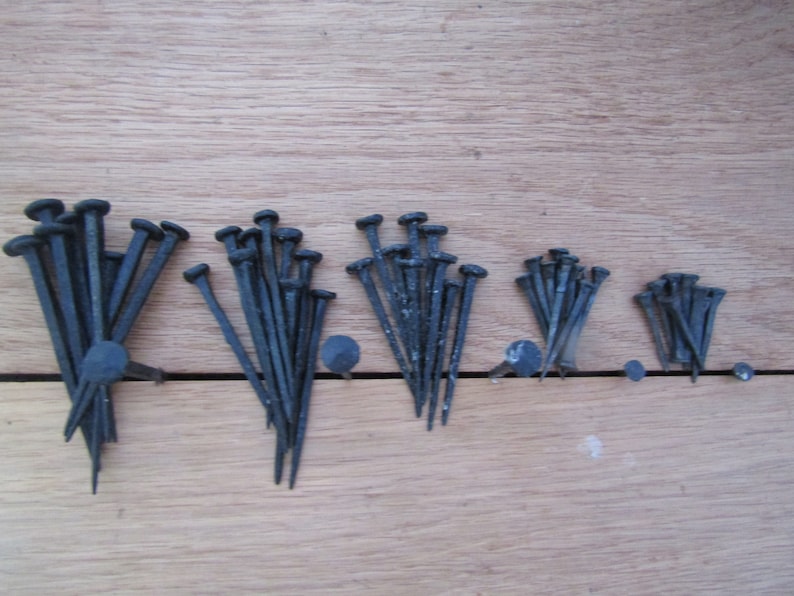 May include: A collection of black metal nails of varying lengths, arranged in rows on a wooden surface.
