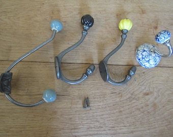 May include: A selection of decorative wall hooks with different knob designs. The hooks have a silver finish and are topped with blue, black, yellow, and blue and white patterned ceramic knobs. Two screws are also visible.