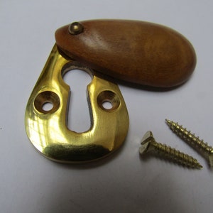 May include: Brass keyhole cover with a wooden escutcheon. The cover is oval shaped and has a small brass knob on the top. Two brass screws are included.