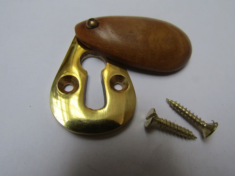 May include: Brass keyhole cover with a wooden escutcheon. The cover is oval shaped and has a small brass knob on the top. Two brass screws are included.